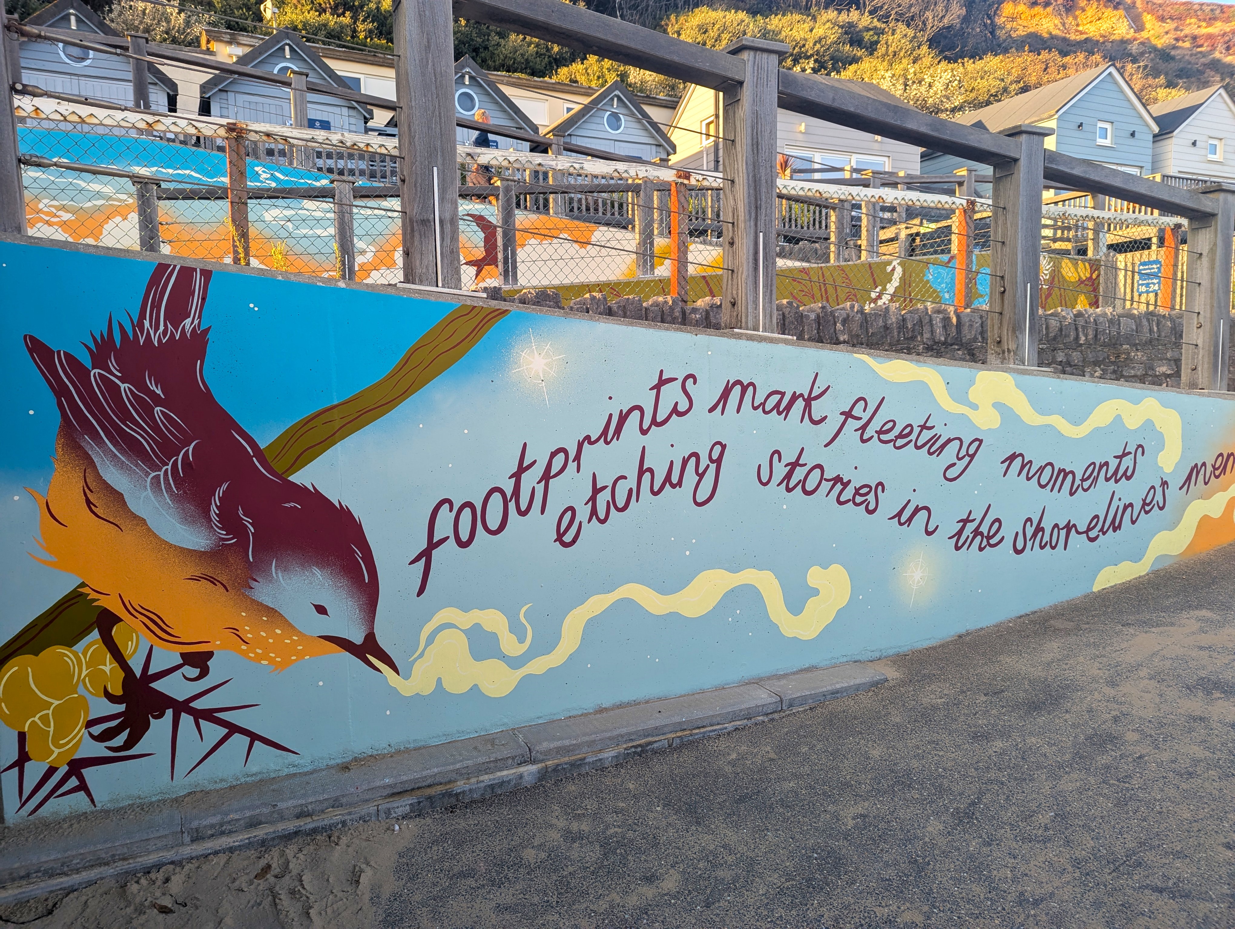 A mural of a bird on a blue background along the edge of the ramp access to the promenade.