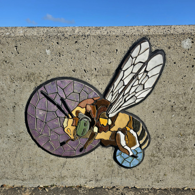 A mosaic rendering of a bee embedded on the coastal wall