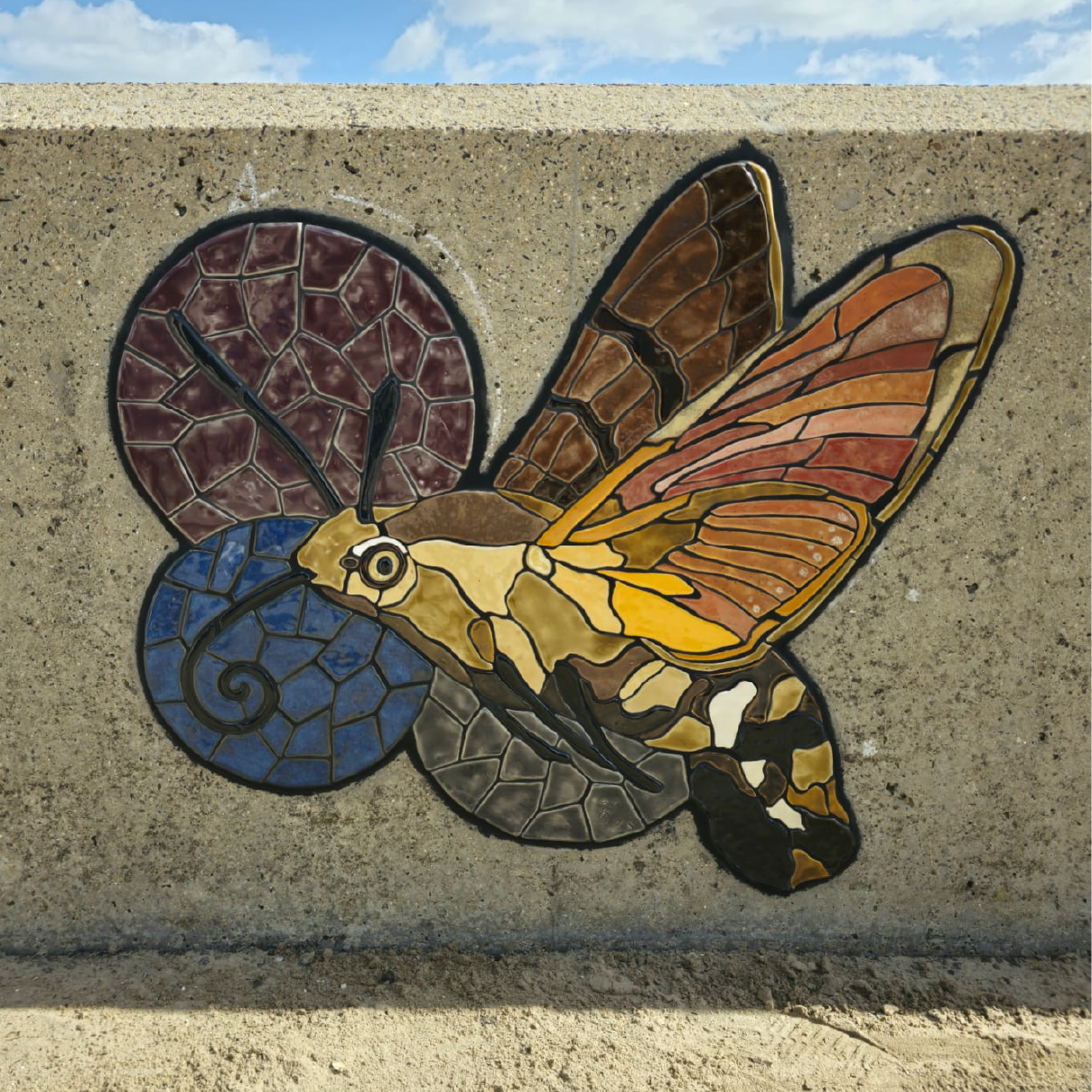 A colourful mosaic of a moth on a low concrete wall.