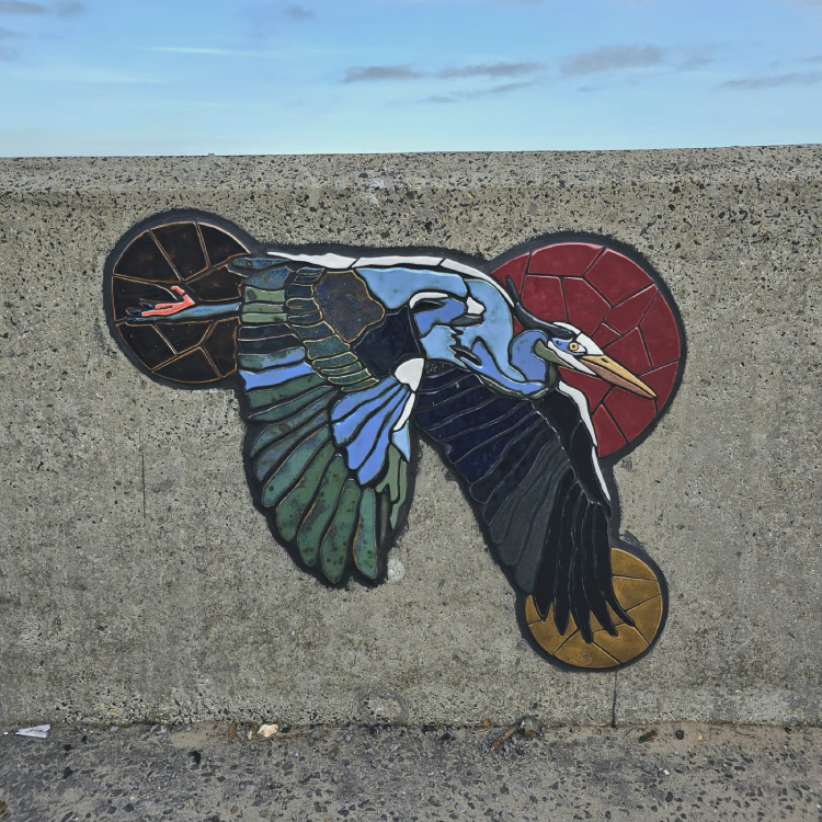 A mosaic rendering of a heron embedded on the coastal wall