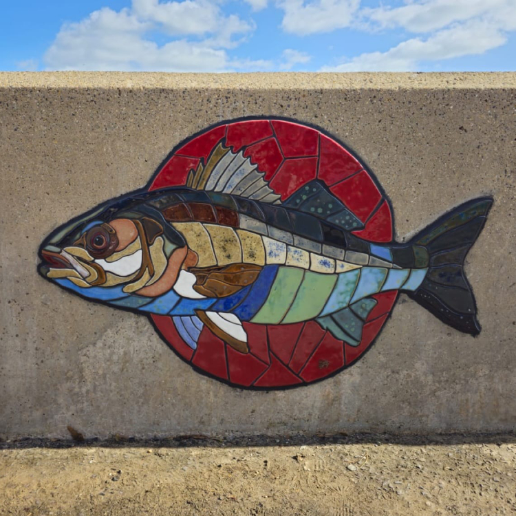 A mosaic rendering of a sea bass embedded on the coastal wall